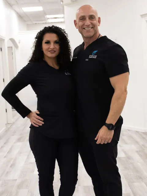 Evolve’s two owners in black Evolve scrubs, smiling, in a bright office hallway